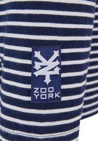 Navy and white striped fabric with a woven logo patch in blue and white, featuring the text "ZOO YORK" and a stylized graphic design.