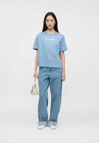 Gaiši zils kokvilnas T-krekls ar apļa kakla izgriezumu, īsām piedurknēm un izšūtu "Tommy Hilfiger" logotipu. Apvienots ar gaiši džinsa platajām biksēm.