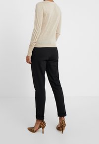 Maglione beige a maniche lunghe, morbido al tatto, con design aderente, abbinato a pantaloni neri su misura. Tacchi a zebre aggiungono un accento audace.