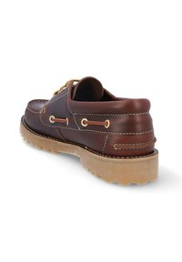 Zapato de barco de cuero marrón con punta redonda, costuras blancas y ojales dorados. Presenta una suela de goma texturizada para mayor tracción.