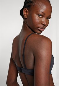 Reggiseno nero con spalline regolabili, tessuto morbido, finitura liscia e chiusura a gancio sul retro. Design semplice e minimalista.