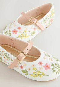 White fabric shoes featuring colorful floral embroidery in pink, yellow, and green, with a pink strap and gold buckle detail.