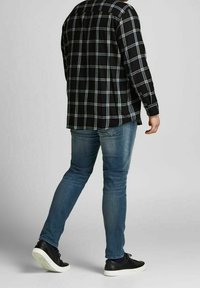 Camicia a scacchi nera con maniche lunghe, jeans in denim blu e sneakers nere. La camicia presenta linee verticali e orizzontali; texture lisce.
