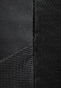 Svart tyg med två texturer: ena sidan har ett slätt, fint nät, medan den andra har ett upphöjt geometriskt mönster.