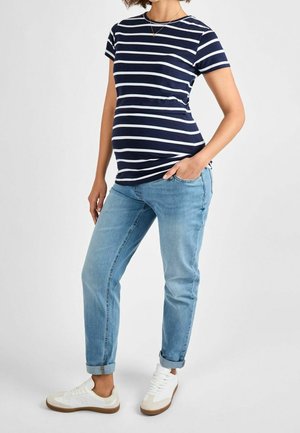 T-shirt ciążowy w niebiesko-białe paski, z krótkim rękawem, dopasowany krój. Noszony z jasnoniebieskimi, podwiniętymi dżinsami oraz białymi trampkami.