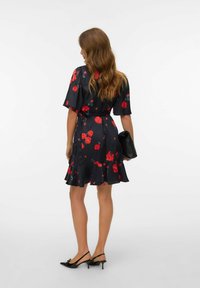 Robe noire à fleurs avec des roses rouges, des manches courtes, un ourlet volanté et une taille nouée. Associée à une pochette noire et des talons pointus.