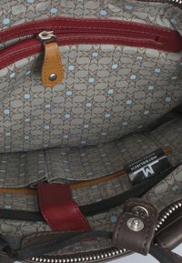 Interieur van een bruine leren tas met een gepatternde grijze voering met bruine en blauwe sterren. Rode rits en accenten met details in lichtbruin leer.