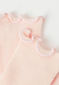 Lyserøde ribbede sokker med en blød, tekstureret overflade, der har en flæsekant øverst og kontrasterende lys lyserøde syninger.