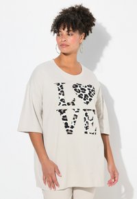 Helle beige Oversized-T-Shirt mit kurzen Ärmeln, auf dem "LOVE" in schwarzen und Leopardenmusterbuchstaben gedruckt ist. Aus weichem Baumwollmaterial, lockere Passform.