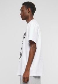 Hvid bomulds t-shirt med korte ærmer og en afslappet pasform. Frontdesignet inkluderer sorte grafikker og tekst, som fremviser en moderne stil.