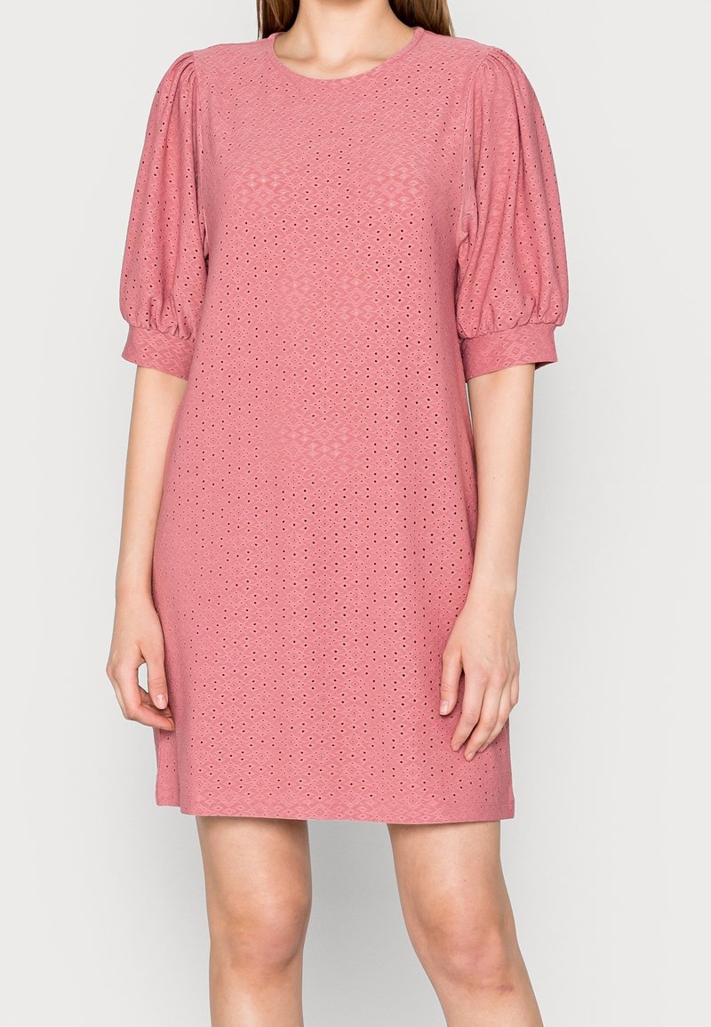 Lyhyt vaaleanpunainen mekko, jossa on puffihihat, pyöreä kaula-aukko ja kyynärpään yksityiskohtia, jotka tuovat tekstiiliin lisärakennetta.