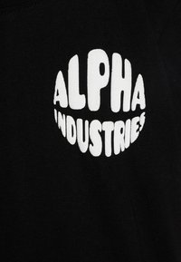 Juodas medvilnės marškinėliai su ryškiu, drąsiu balto "ALPHA INDUSTRIES" logotipu apvalioje formoje. Minkšta tekstūra, klasikinis fasonas.