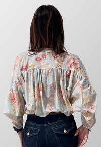 Blusa floreale azzurro chiaro con vestibilità morbida, caratterizzata da un retro arricciato, maniche lunghe a sbuffo e una texture morbida e leggera.
