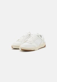 Balti sportiniai bateliai su lygaus odos viršumi, perforuota nėrimo dalimi ir šviesiai rudos spalvos guminėmis apačiomis su tekstūruotu dizainu.