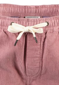 Pantaloni corti in corduroy rosa con vita regolabile da un laccetto bianco e occhielli argentati. Il tessuto presenta una texture a righe.