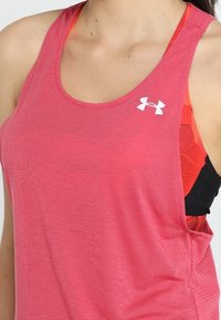 Gros plan d'une personne portant un haut de sport sans manches rose Under Armour par-dessus un soutien-gorge de sport orange.