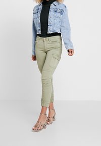 Avkortad jeansjacka i ljusblått, olivgröna cargobyxor med fickdetaljer, och beige remsandaler med hög klack och ormskinnsmönster.