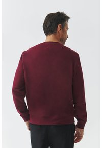 Sudadera burdeos con cuello redondo y mangas largas. Tejido suave, corte relajado, puños y dobladillo de canalé, detalle de costura mínima en la parte trasera.