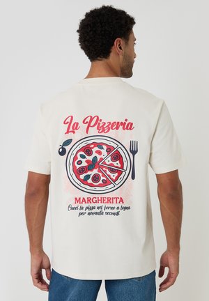 Mand iført hvid T-shirt med pizzaillustration, gaffel og tekst om tilberedningsvejledning for Margherita-pizza på italiensk på ryggen.