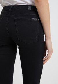 Jeans de mezclilla negra con un diseño ajustado, con un corte de cinco bolsillos y una etiqueta de logo cosida en la parte trasera de la cintura.