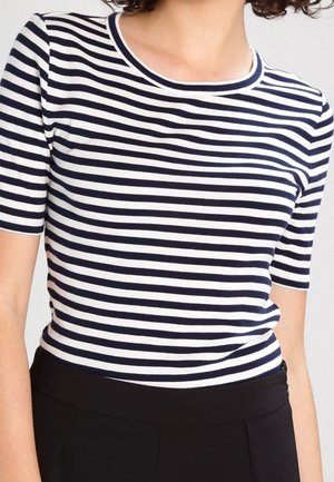 Femme portant un haut à manches courtes à rayures bleu marine et blanches, rentré dans un pantalon noir taille haute, vue des épaules à la taille.