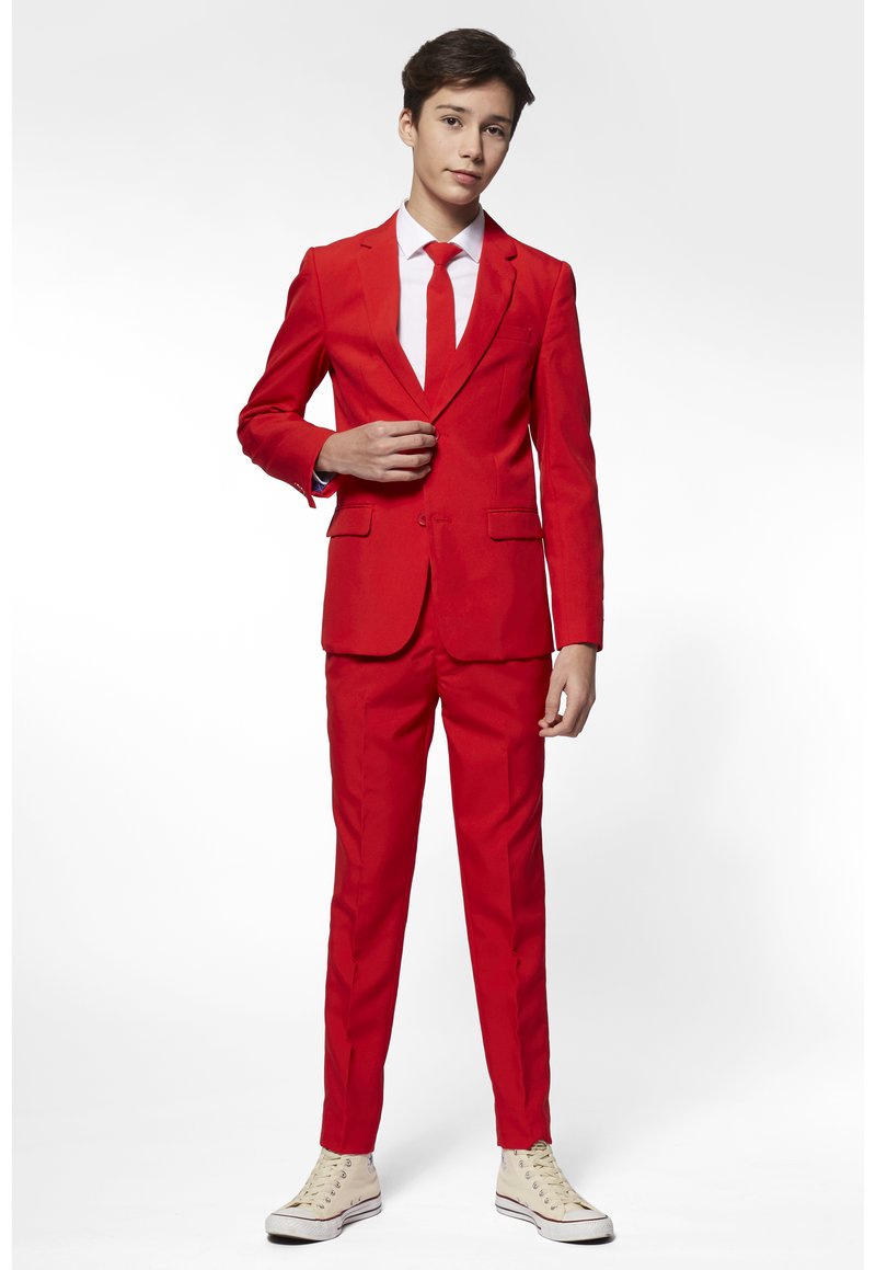 Completo rosso con cravatta, camicia bianca, design slim fit, blazer con un bottone, pantaloni flat front, abbinati a sneakers beige. Tessuto dalla texture liscia.