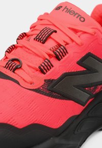 Baskets de sport rouge vif avec des accents noirs, logo "N" noir et lacets rouges enfilés à travers des œillets à rayures noires.