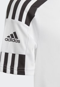 Camiseta deportiva blanca con diseño de tres rayas negras en las mangas, con un logotipo de Adidas bordado en negro en el hombro izquierdo.