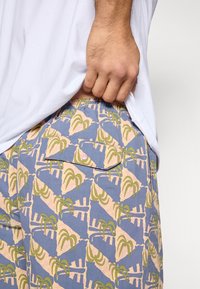 Μπλε σορτς με επαναλαμβανόμενο σχέδιο φοίνικα και αφηρημένα μοτίβα σε ροζ και πράσινο. Ελαστική μέση και εμφανές πλάγιο τσέπη.