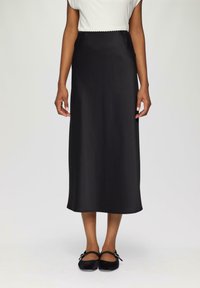 Schwarzer Satin-Maxi-Rock mit glatter Textur und elastischem Bund, kombiniert mit schwarzen Ballerinas mit Knöchelriemen.