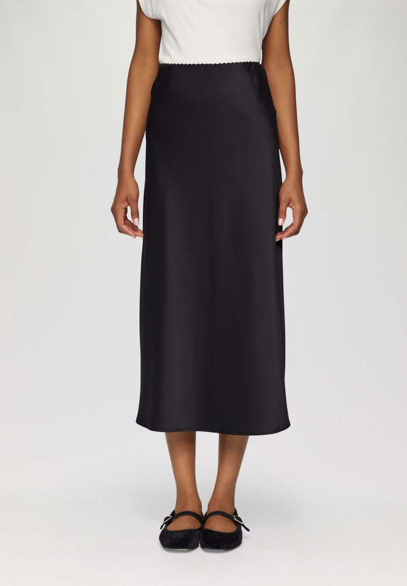 Schwarzer Satin-Maxi-Rock mit glatter Textur und elastischem Bund, kombiniert mit schwarzen Ballerinas mit Knöchelriemen.