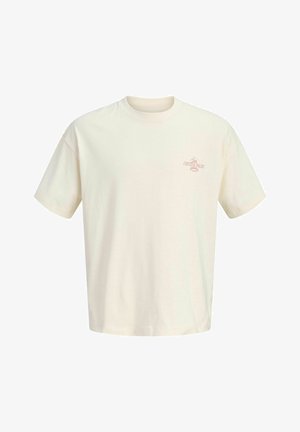 Chłopiec stoi, ubrany w kremowy T-shirt, ciemne dżinsowe szorty, kremowe trampki, sportowe skarpetki oraz czerwoną czapkę z daszkiem na jednolitym tle.