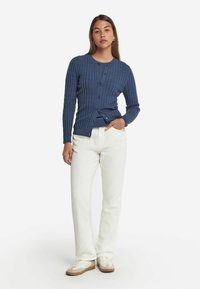 Granatowy kardigan prążkowany z długim rękawem i zapięciem na guziki, zestawiony z białymi prostymi spodniami i jasnymi trampkami.