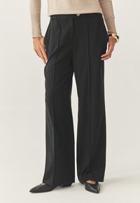 Pantaloni neri a gamba larga con fronte piatto e due tasche laterali, realizzati in un tessuto liscio; abbinati a ballerine nere a punta.