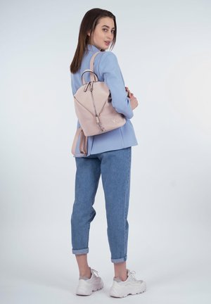 Sac à dos en cuir rose de forme triangulaire, avec deux poignées supérieures et des bretelles réglables. Il dispose d'une fermeture éclair et d'un discret logo.