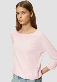 Top à manches longues rose clair avec un col rond, fabriqué en tissu doux, présentant une coupe décontractée et une texture subtile. Associé à un short en denim.