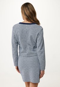 Blå och vit mönstrad klänning med l�ånga ärmar, figursydd form och marinblå krage. Den texturerade tyget skapar ett rutmönster över ytan.