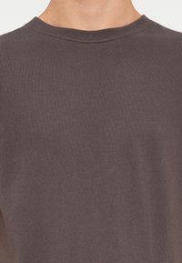 Camiseta de algodón de color gris oscuro con cuello redondo, mangas cortas y una textura suave y lisa. Diseño sencillo sin patrones ni adornos.