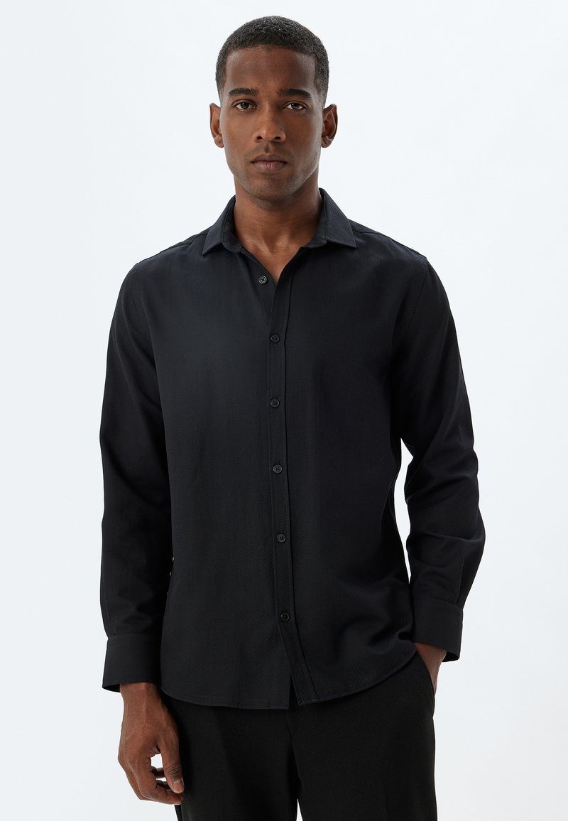 Zwarte blouse met lange mouwen, gemaakt van gladde stof, met een knopenlijst aan de voorkant, puntige kraag en enkele manchetten. Eenvoudig, klassiek ontwerp.
