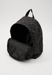 Zaino nero con un motivo geometrico in una tonalità più chiara. Tessuto morbido, forma arrotondata, chiusura con zip e maniglia superiore per il trasporto.