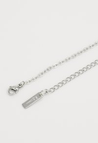 Pulsera de cadena de plata con eslabones ovalados, un cierre de langosta y una etiqueta rectangular con un diseño grabado en un lado.