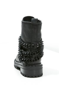 Svart läderankelboot med en texturerad yta, som har framträdande svarta piggar runt midjan och en mönstrad gummisula.