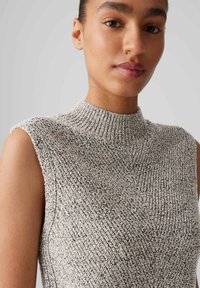 Lightweight, sleeveless, high-neck top in a textured, knitted fabric with a neutral color palette of gray and off-white speckles.