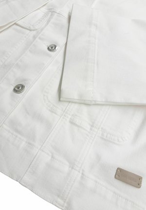 Biała kurtka jeansowa zbliżenie pokazujące metalowe guziki i naszywane kieszenie, z podwiniętym rękawem i małą beżową metką na dole.