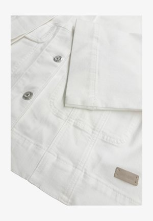 Baltas džinsa jaka tuvplānā, redzamas metāla pogas un šūtas kabatas, ar salocītu piedurkni un nelielu bēša krāsas etiķeti apakšmalā.