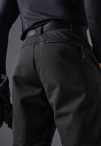 Pantalones cortos deportivos negros con una textura suave, que cuentan con un bolsillo trasero con cremallera y una cinturilla elástica ancha, mostrados desde un ángulo trasero.