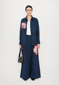 Camicia oversize blu navy e pantaloni a gamba larga con dettagli a stampa floreale. Tessuto morbido, design con colletto, abbinati a una borsa a spalla nera.