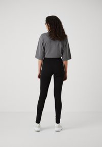 T-shirt gris oversize, coupe ample, associé à des leggings noirs taille haute. Modèle portant des chaussures de sport blanches. Design minimaliste, couleurs unies.