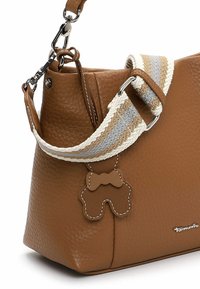 Brązowa torebka ze skóry o fakturze, z plecionym paskiem w beżowe i szare paski oraz małym, jasnobrązowym zawieszonym breloczkiem w kształcie misia.