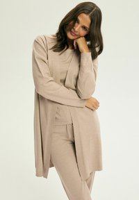 Jasno beżowy sweter z dzianiny z otwartym przodem, długimi rękawami i ściągaczowymi detalami, zestawiony z pasującą bluzką i spodniami o miękkiej fakturze.